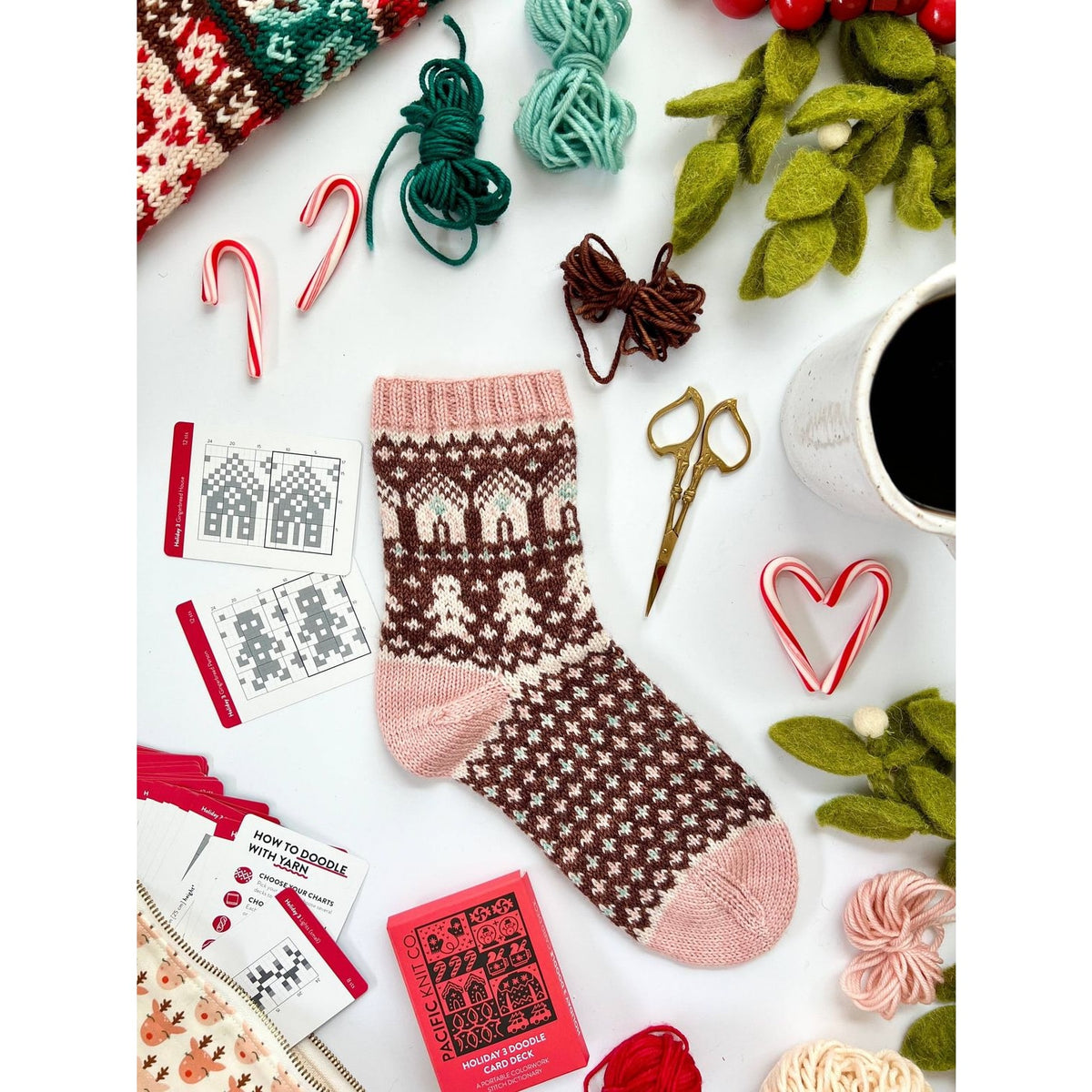 Cozy brown and pink knitted sock surrounded by craft supplies, featuring Christmas holiday cards nearby
