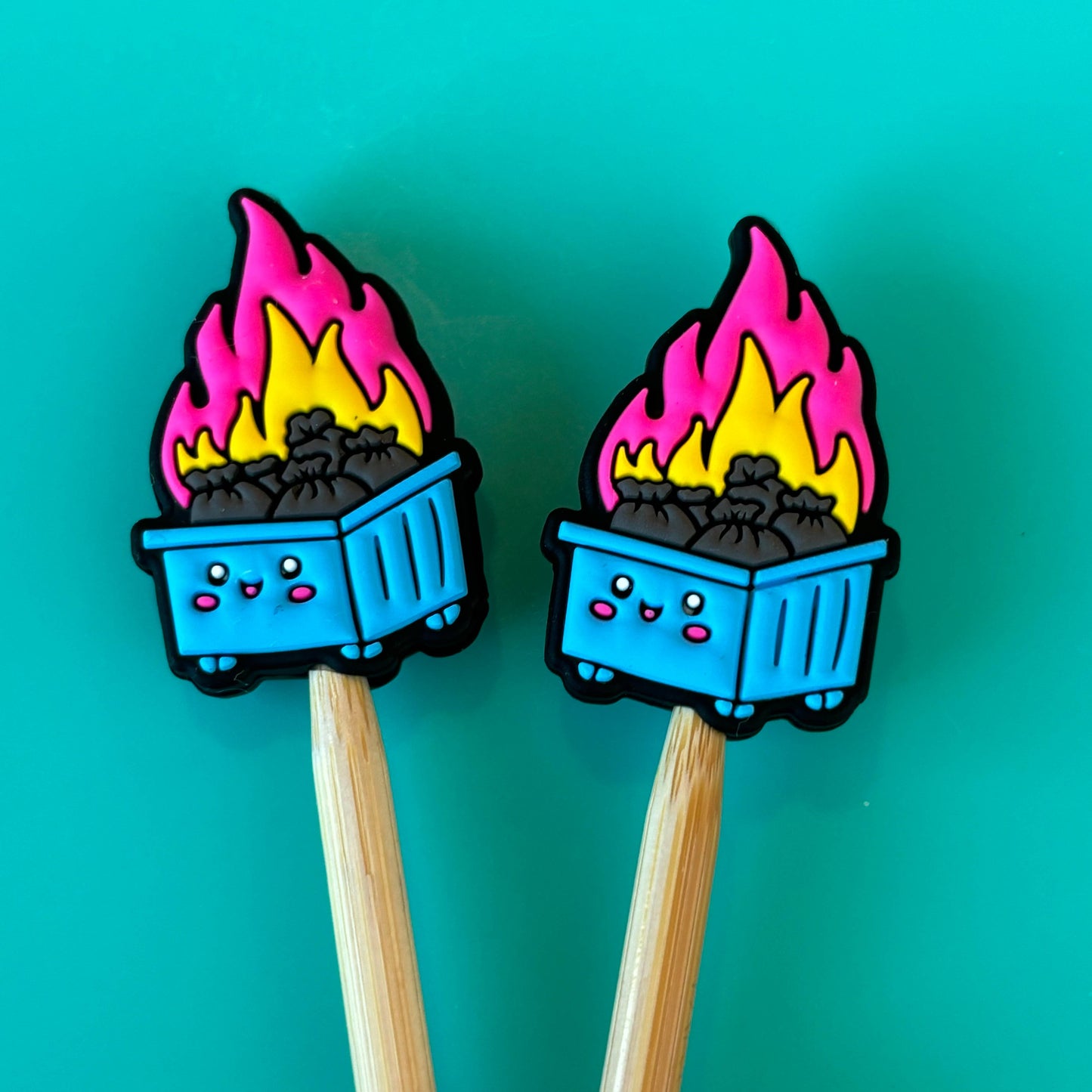 Comma Craft Co colorful dumpster fire knitting needle point protectors shown as a pair on wooden needles on teal background