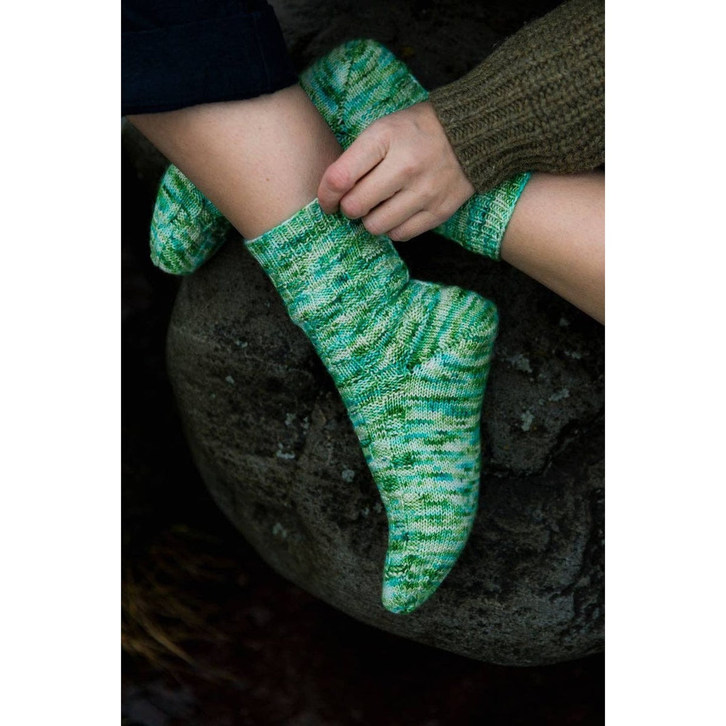 Soothing Stitches knitting book featuring vibrant green hand-knit socks on a stone surface