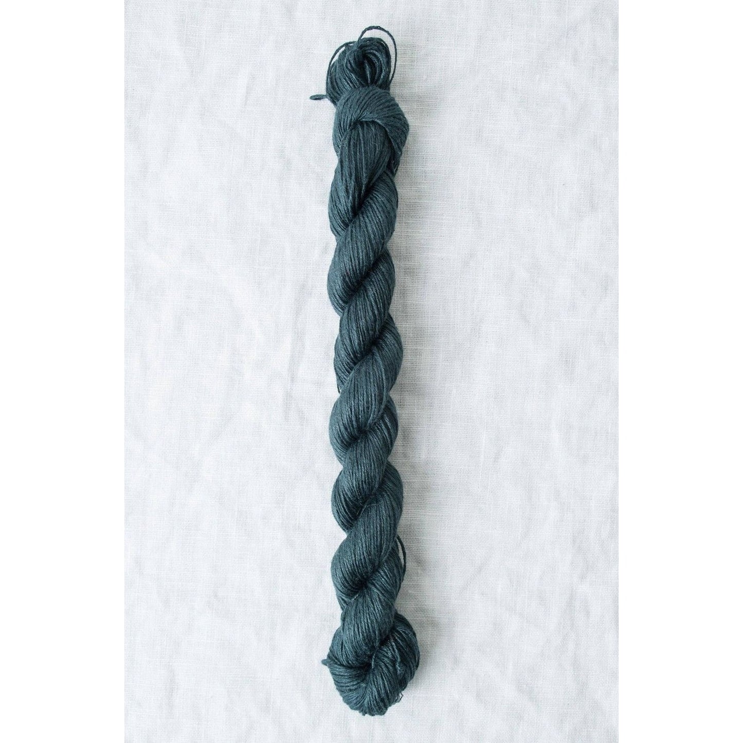 Skein of Sparrow organic linen yarn in deep teal color, ideal for knitting and crochet projects