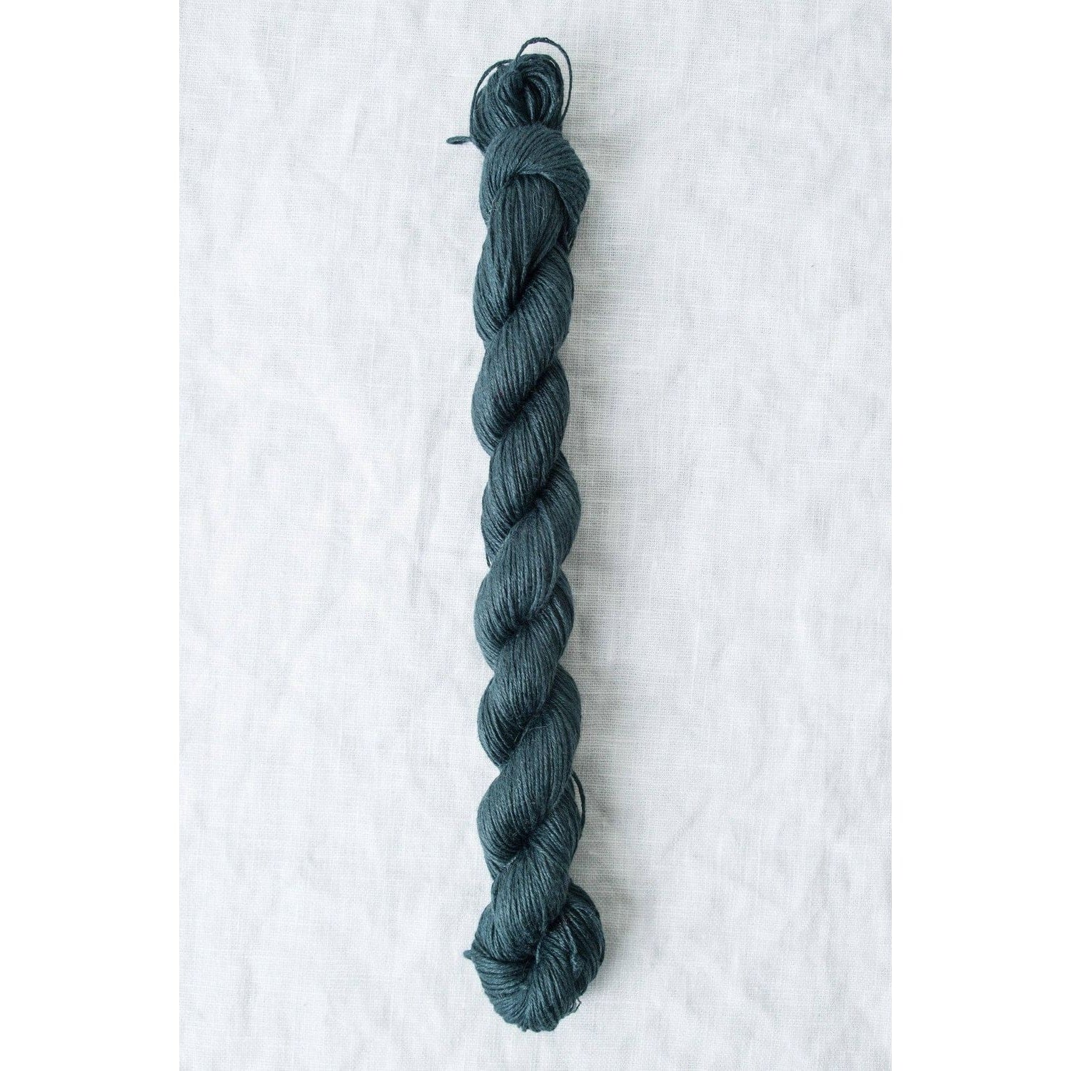 Skein of Sparrow organic linen yarn in deep teal color, ideal for knitting and crochet projects
