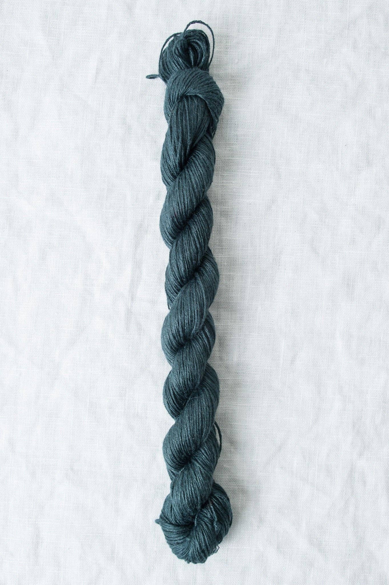 Skein of Sparrow organic linen yarn in deep teal color, ideal for knitting and crochet projects