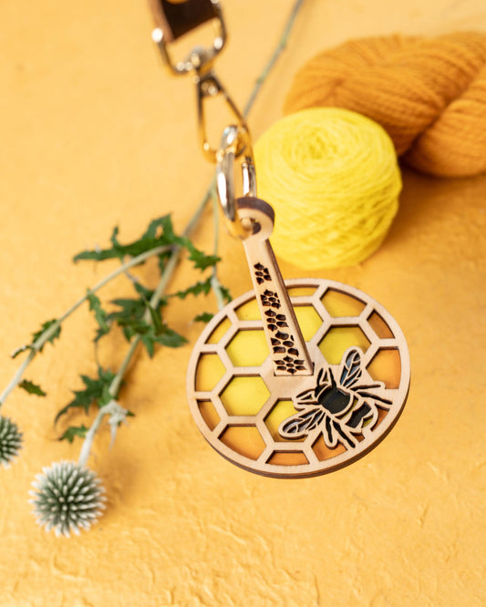 Lemonwood wooden bee knitting accessory keychain with honeycomb pattern and yellow yarn background