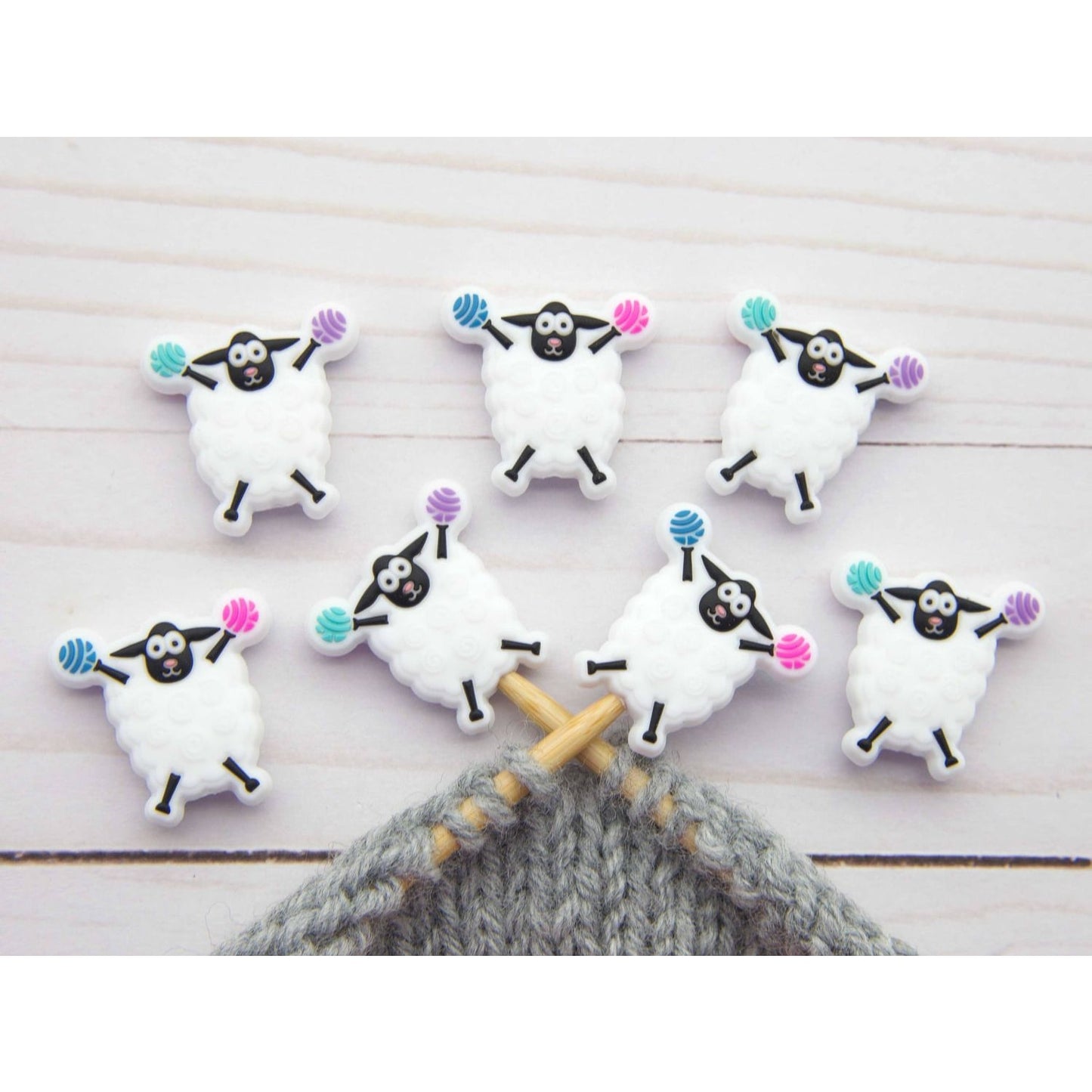 Fox and Pine Stitches sheep stitch markers with pastel yarn balls on knitting needles and gray knit swatch