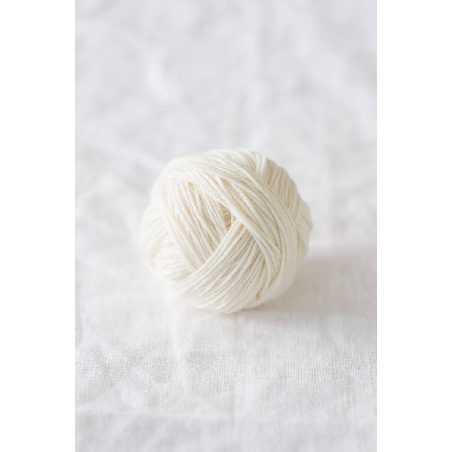 Quince & Co. superwash merino fingering yarn ball in natural white color on white fabric background