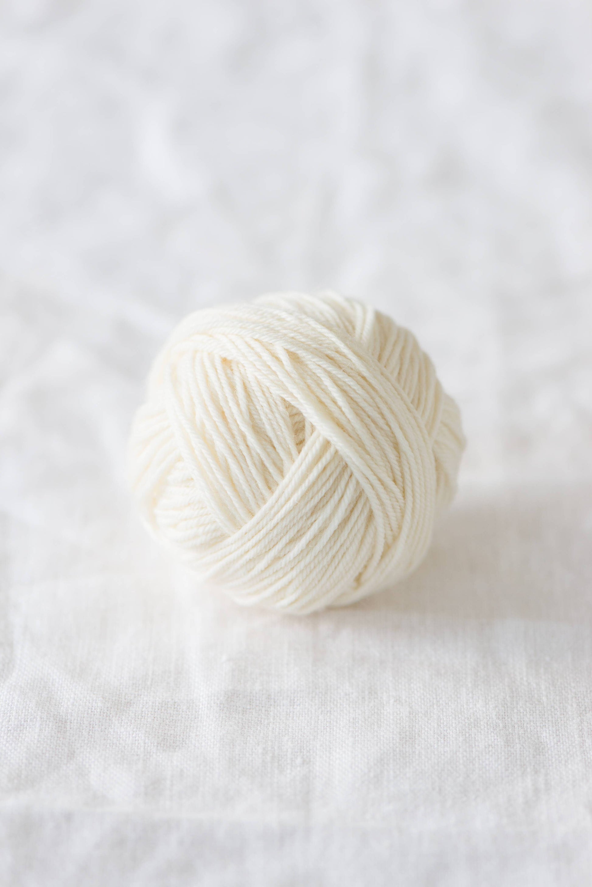 Quince & Co. superwash merino fingering yarn ball in natural white color on white fabric background
