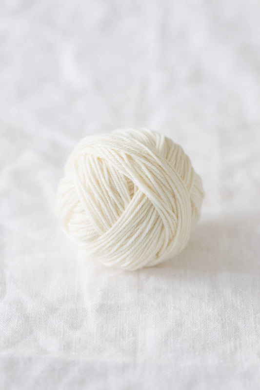 Quince & Co. superwash merino fingering yarn ball in natural white color on white fabric background