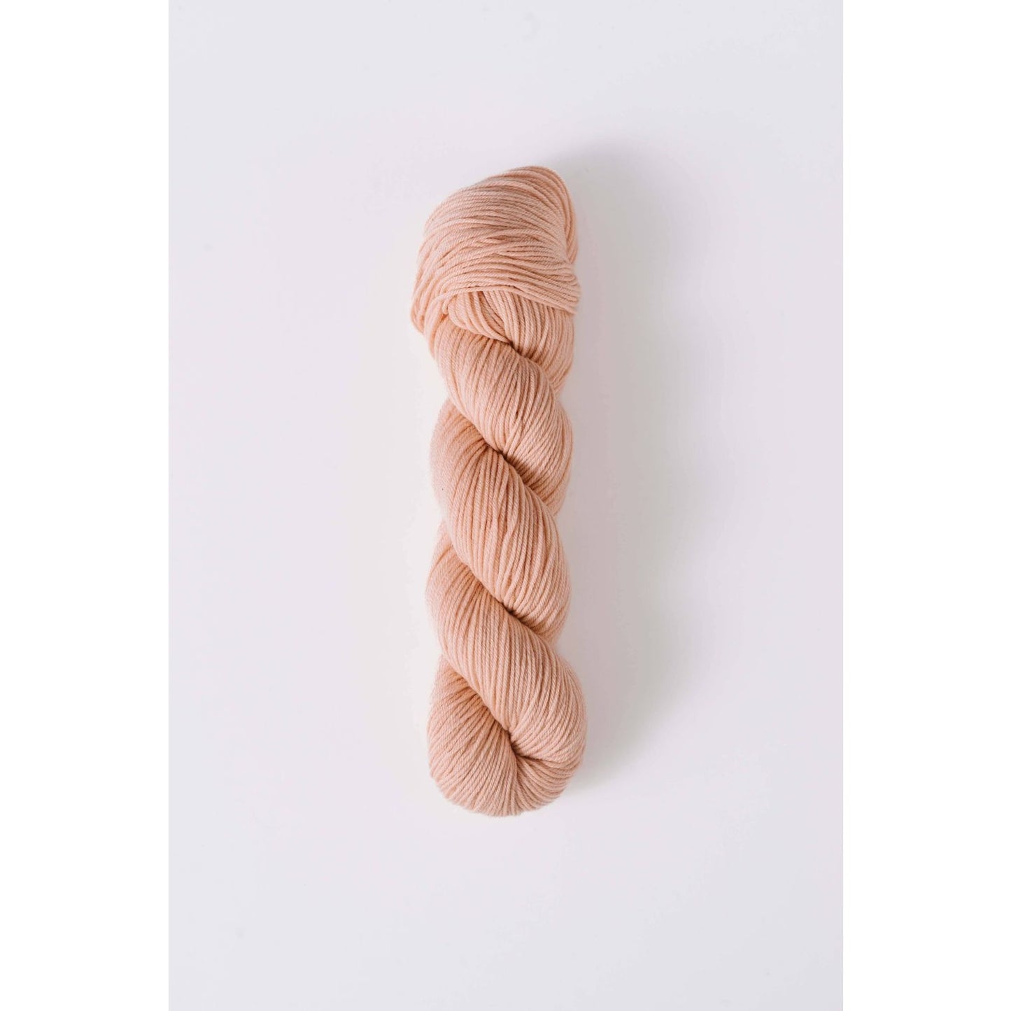 Quince & Co. soft peach colored superwash merino fingering yarn skein isolated on white background