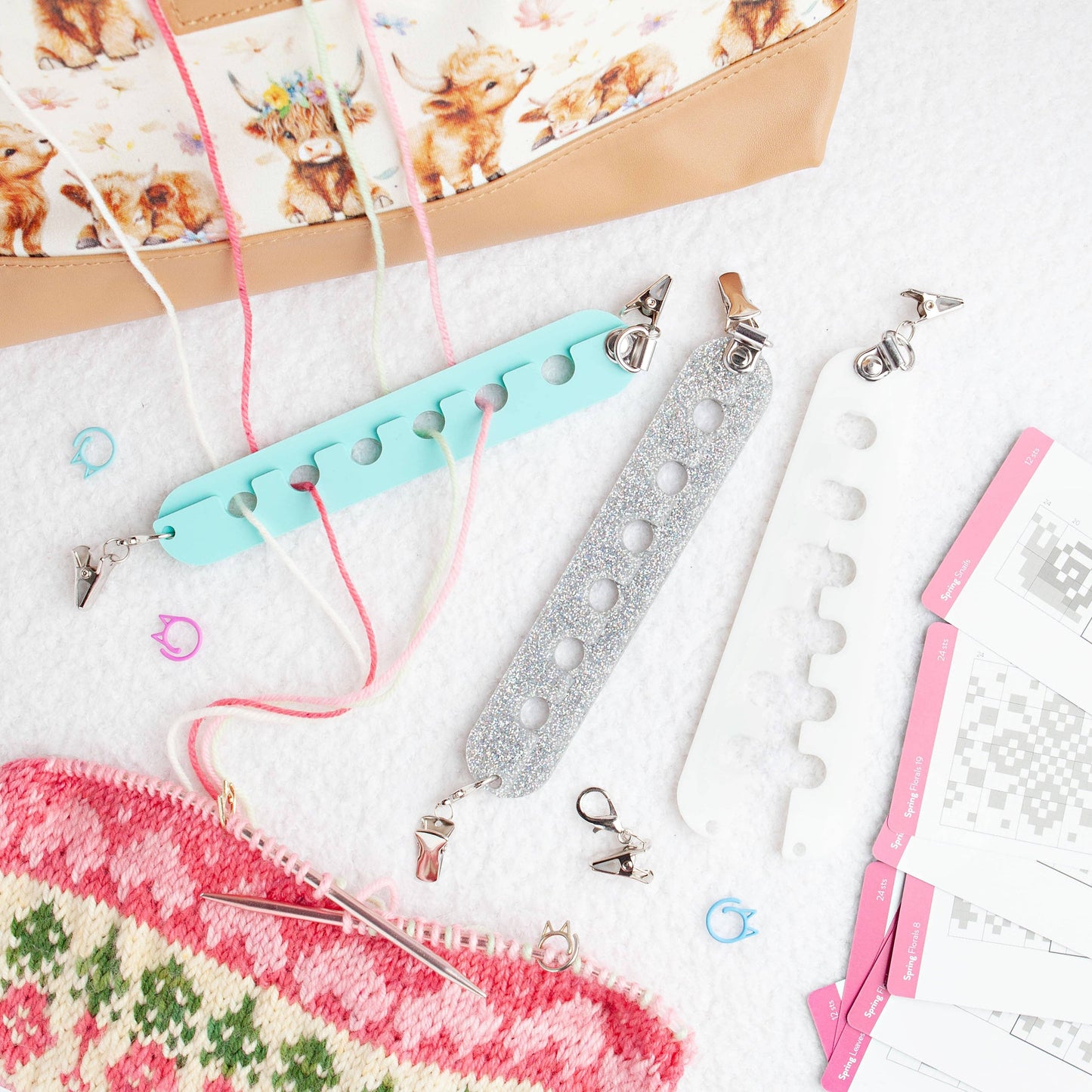 Colorful yarn organizer tools with clips and yarn threads beside a patterned knitting bag