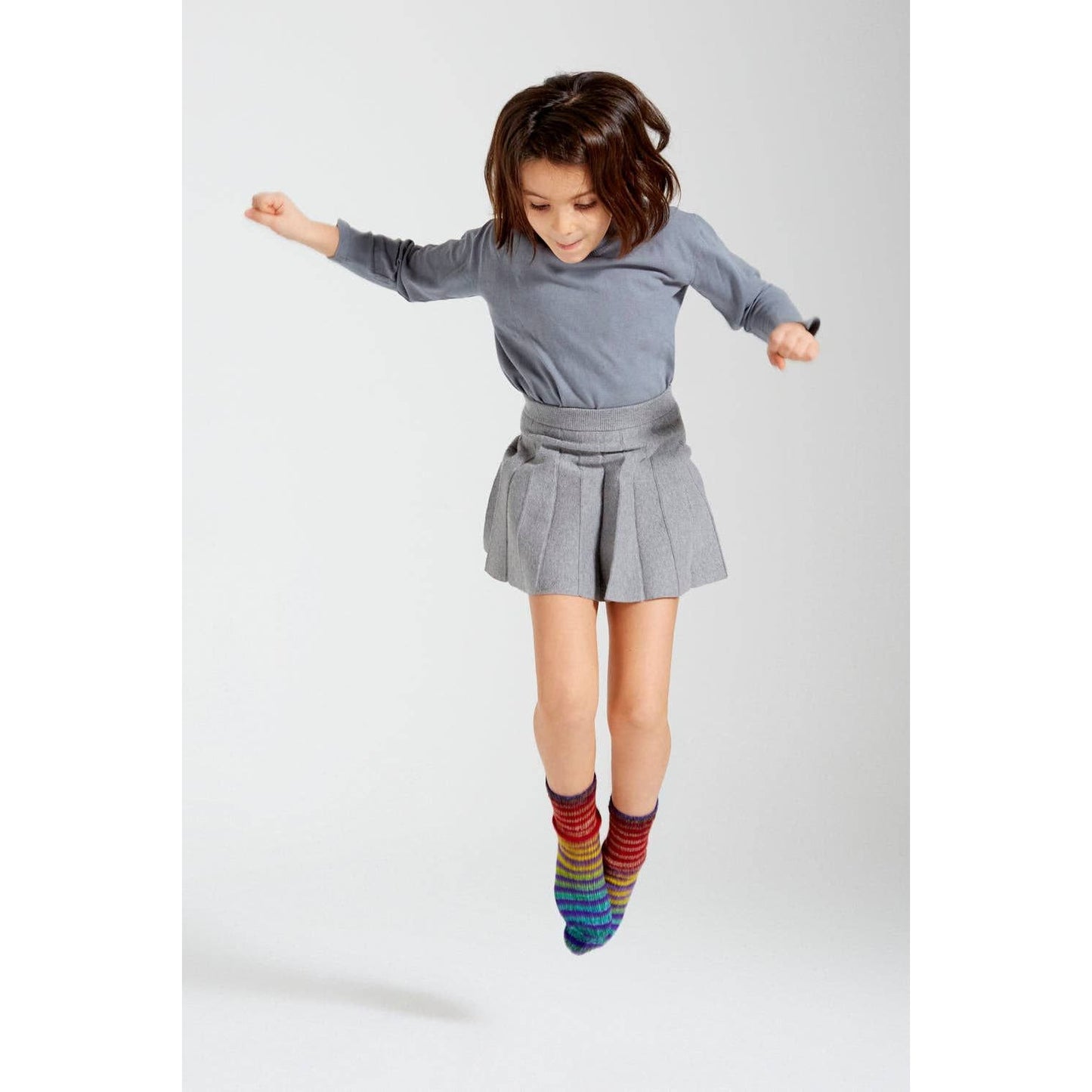 Child wearing colorful socks made from Urth Yarns Uneek Sock Kit Mini, jumping in a playful pose