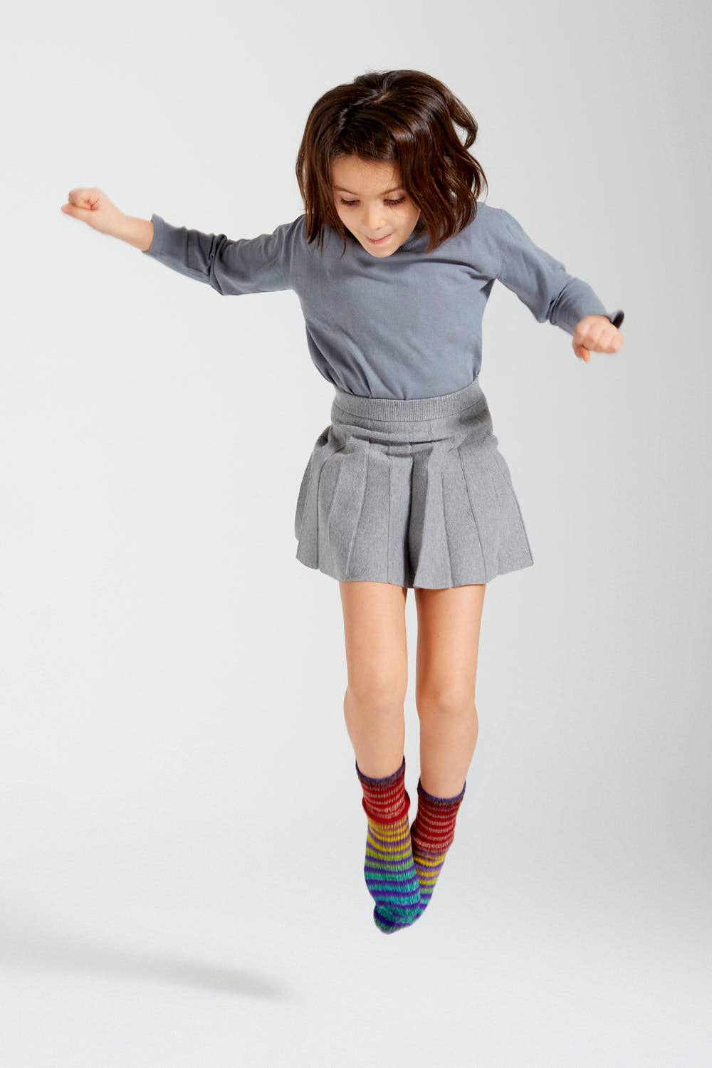 Child wearing colorful socks made from Urth Yarns Uneek Sock Kit Mini, jumping in a playful pose