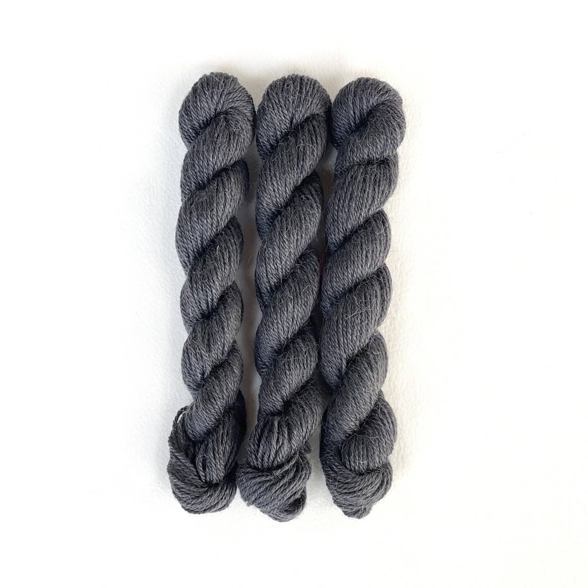 Three skeins of Kelbourne Woolens Perennial Minis yarn in a rich gray color for crafting projects