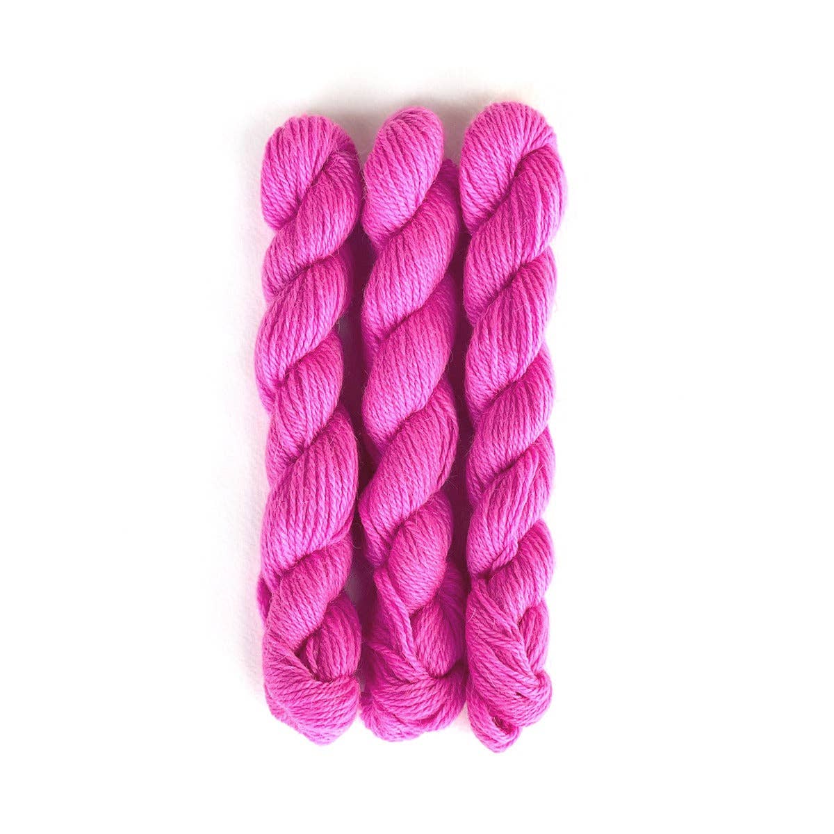 Three skeins of vibrant pink Perennial Minis yarn by Kelbourne Woolens for knitting and crochet projects