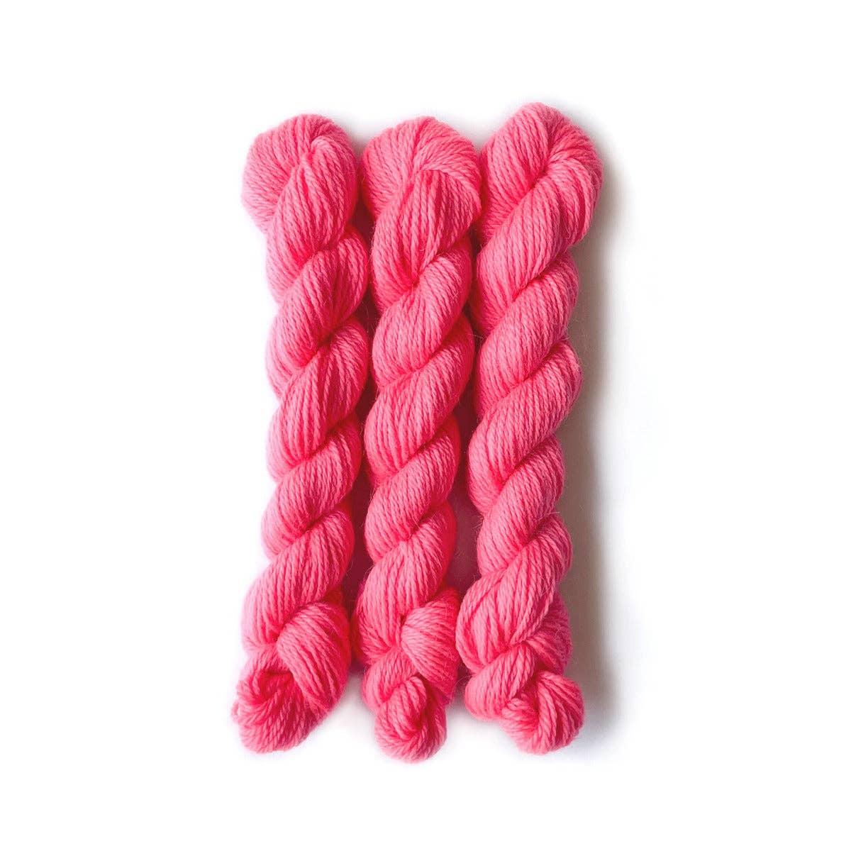 Three skeins of vibrant pink Kelbourne Woolens Perennial Minis yarn for various knitting projects