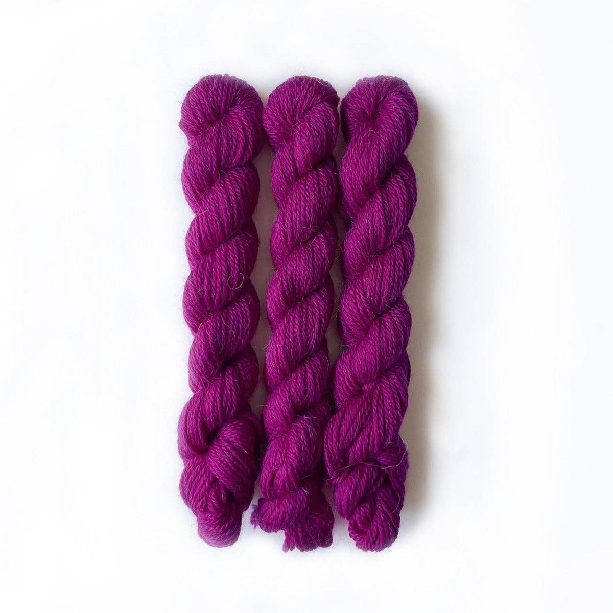 Three skeins of Kelbourne Woolens Perennial Minis yarn in vibrant purple for knitting and crafting