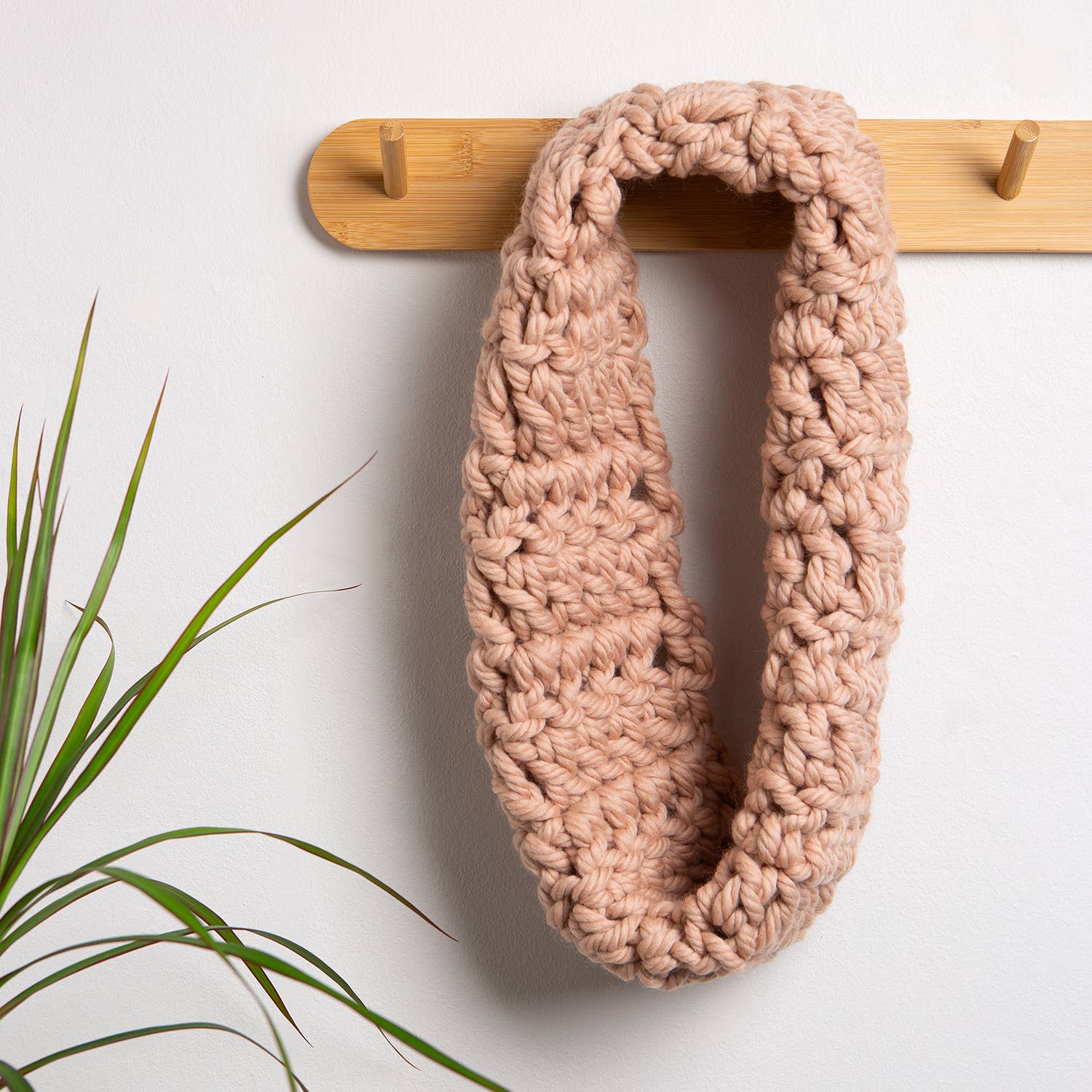 Wool Couture Company beginner crochet cowl kit chunky blush infinity cowl hanging on wooden peg rack for cozy winter