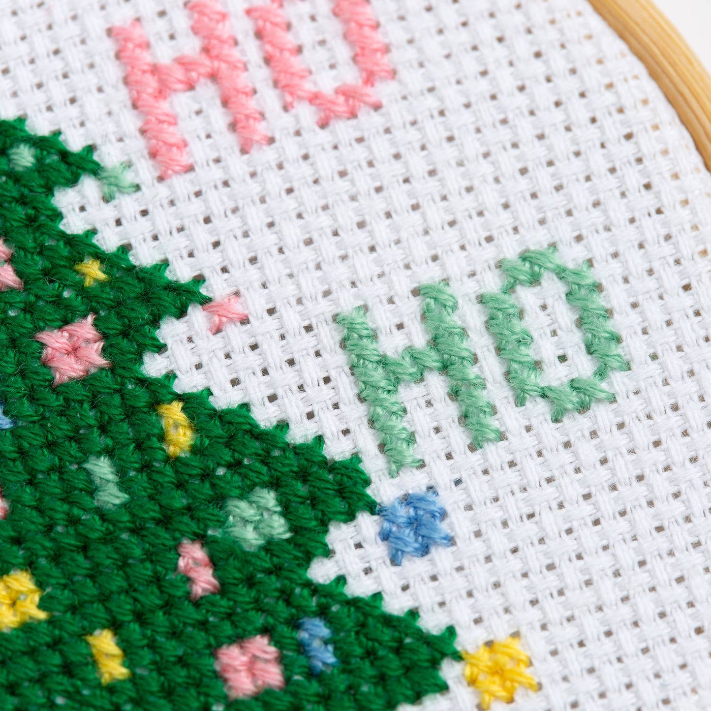 Christmas tree cross stitch kit showing close up of green stitched tree with colorful ornaments on white Aida fabric